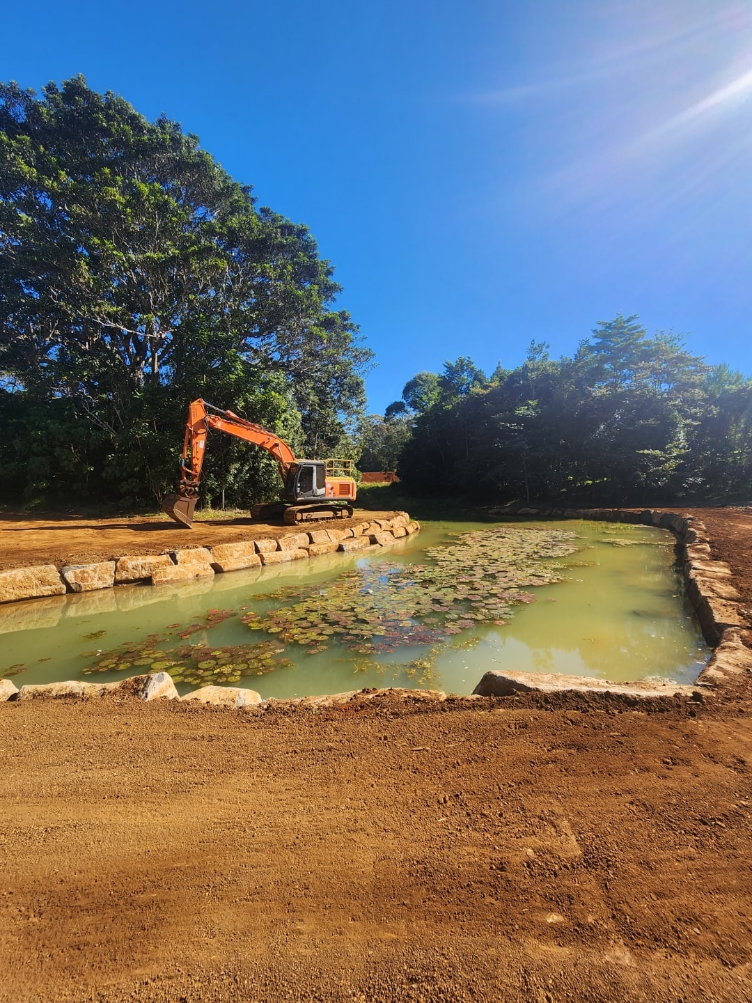 Excavator beside a finished pond with stone edging